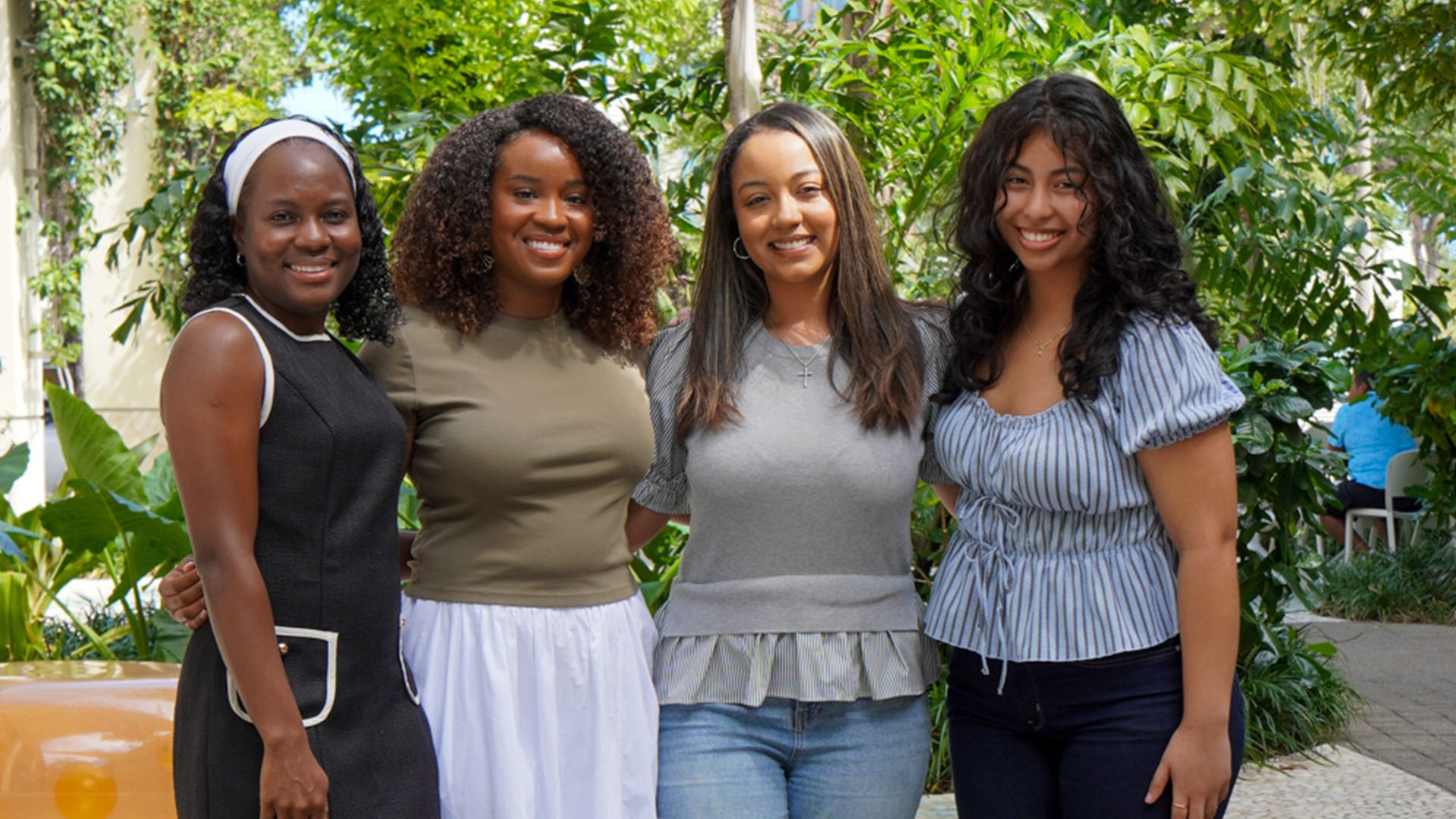 Four women smile together outdoors.
