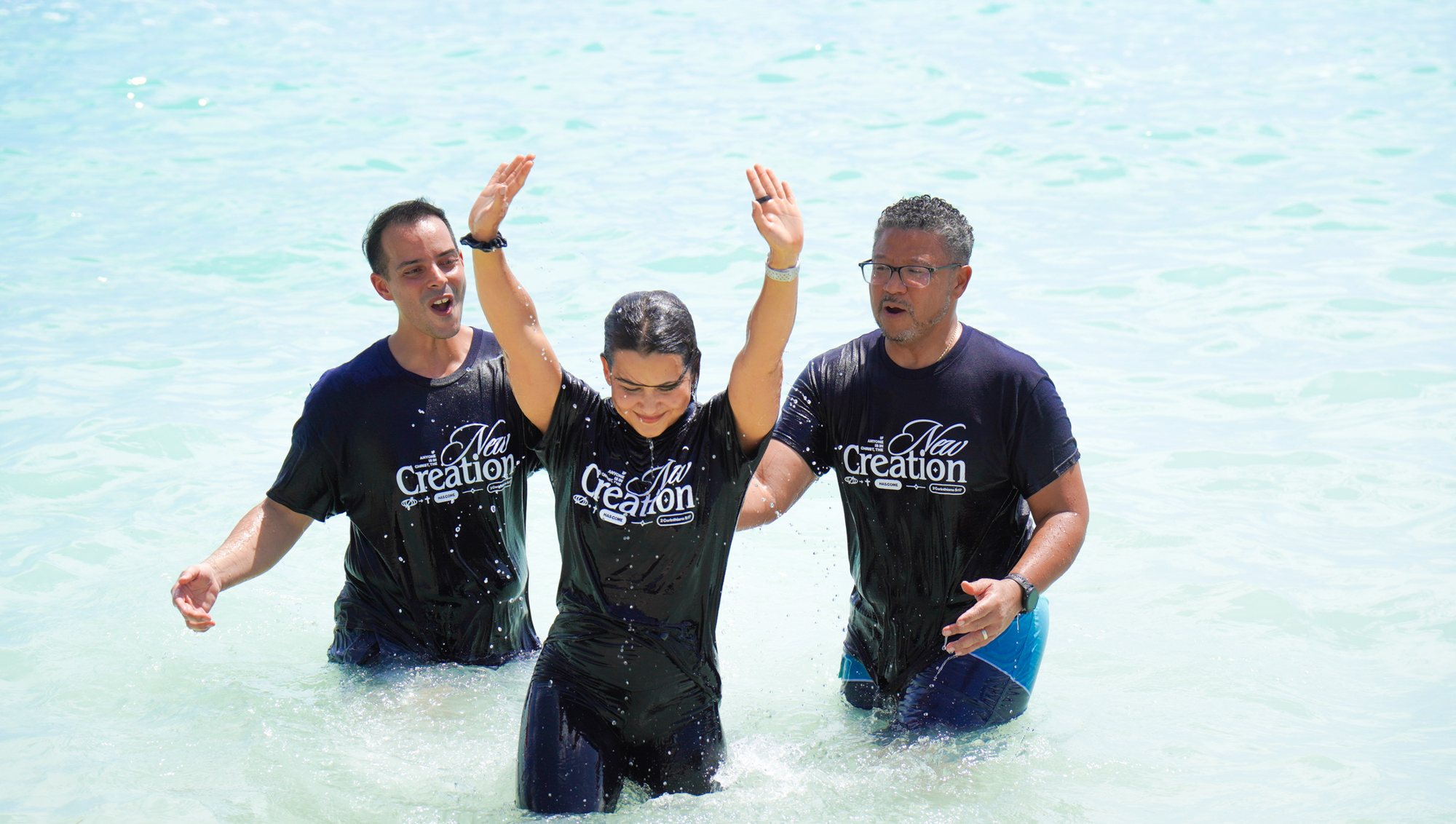 A person raises their hands during a baptism in the sea.