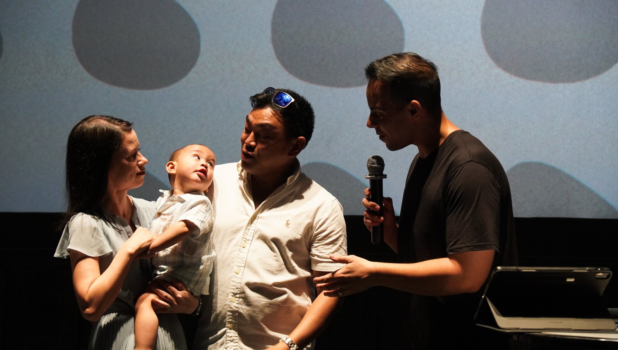 Adults hold a baby while a speaker addresses them during a dedication.