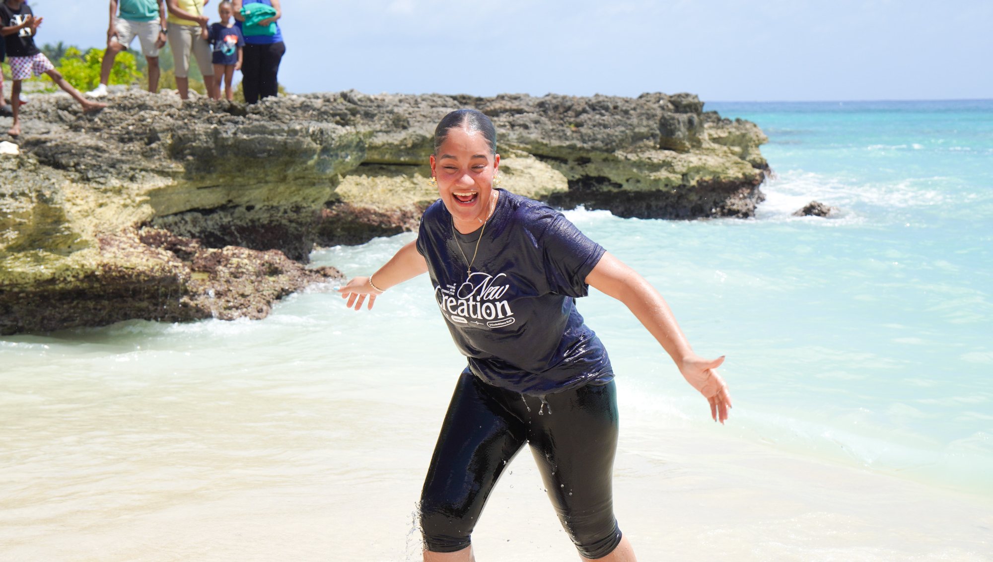 A smiling person steps through the shallow seawater after a baptism.