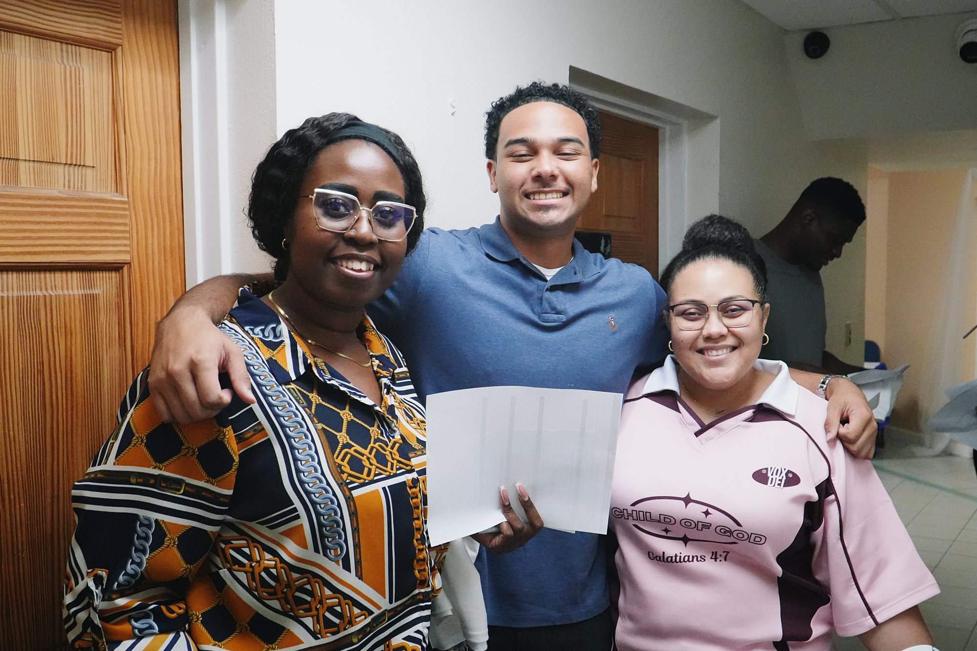 Three people smile together near a doorway at a church gathering.