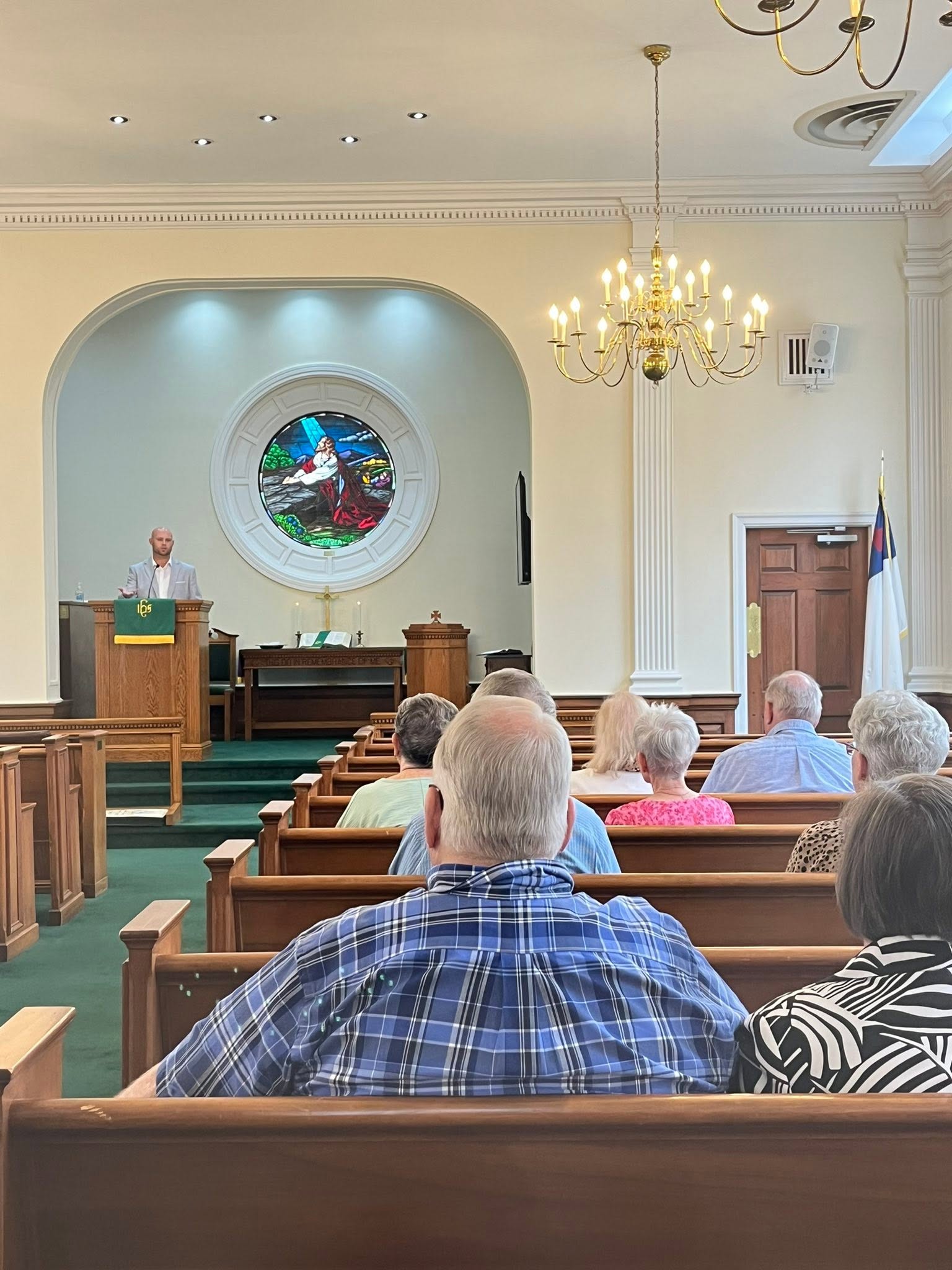 Open doors looking into worship at Anniston First, with people talking between the pews.