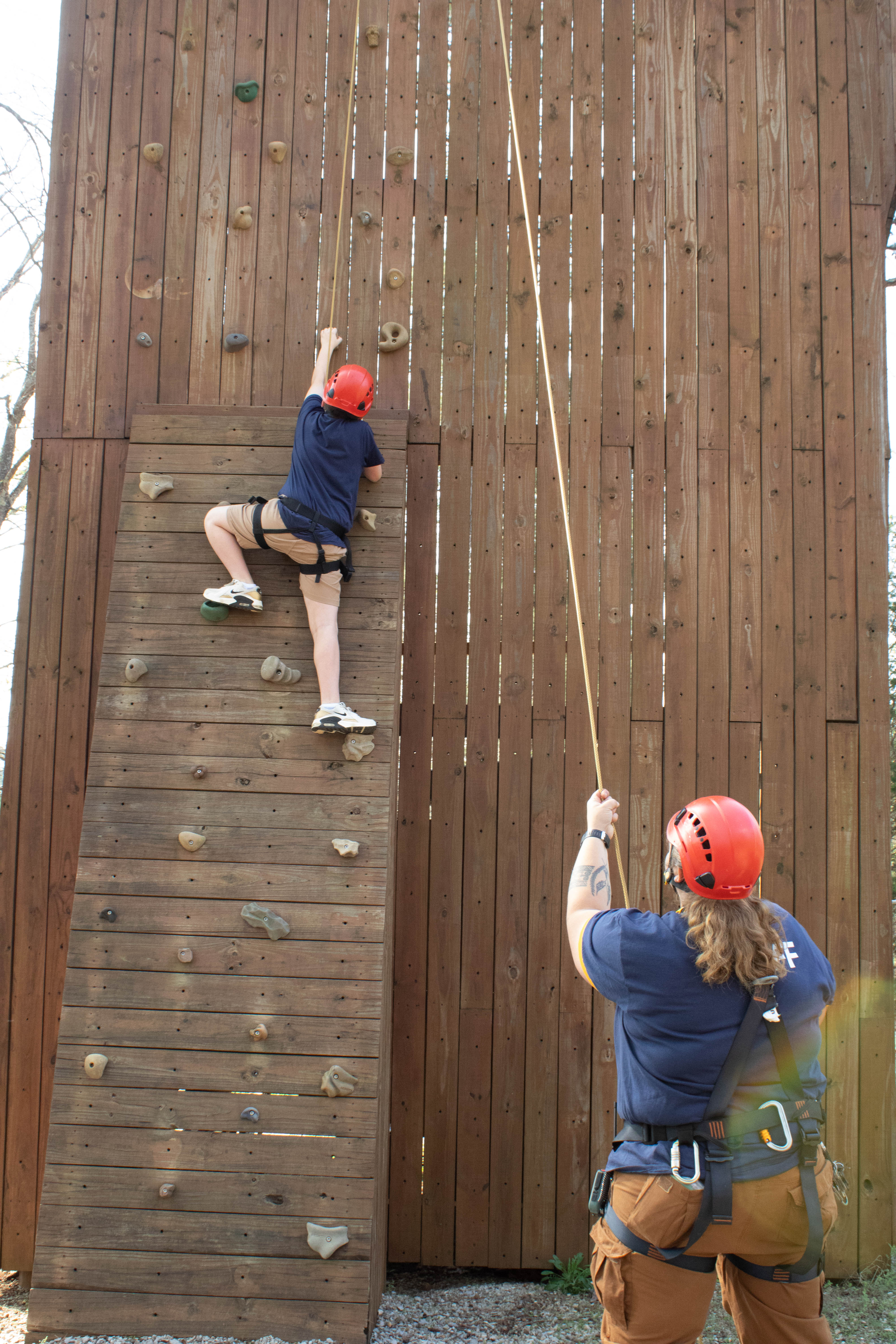 A camper on the climbing wall with a staff member belaying below