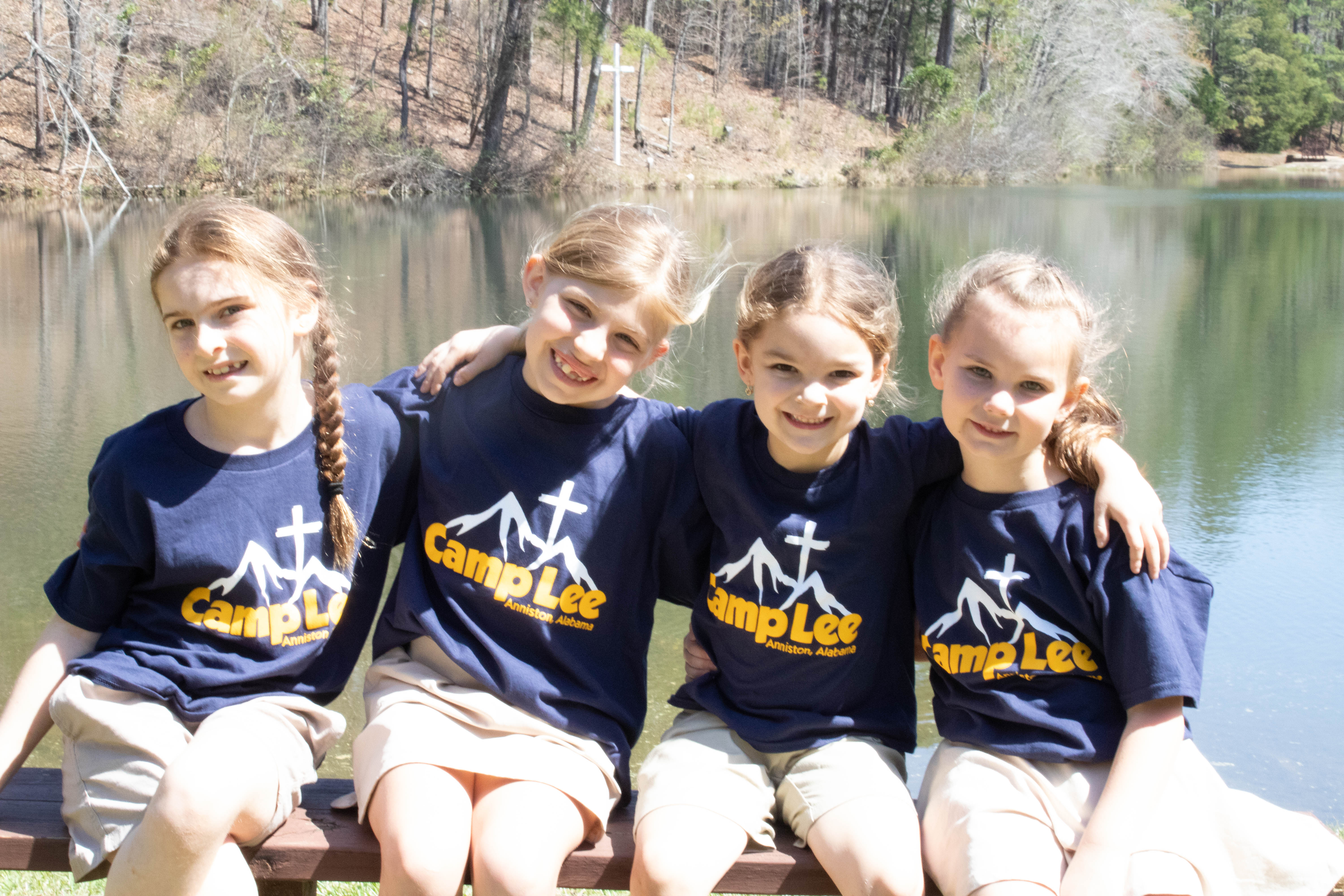 Four day campers sitting together by the lake with their arms around each other