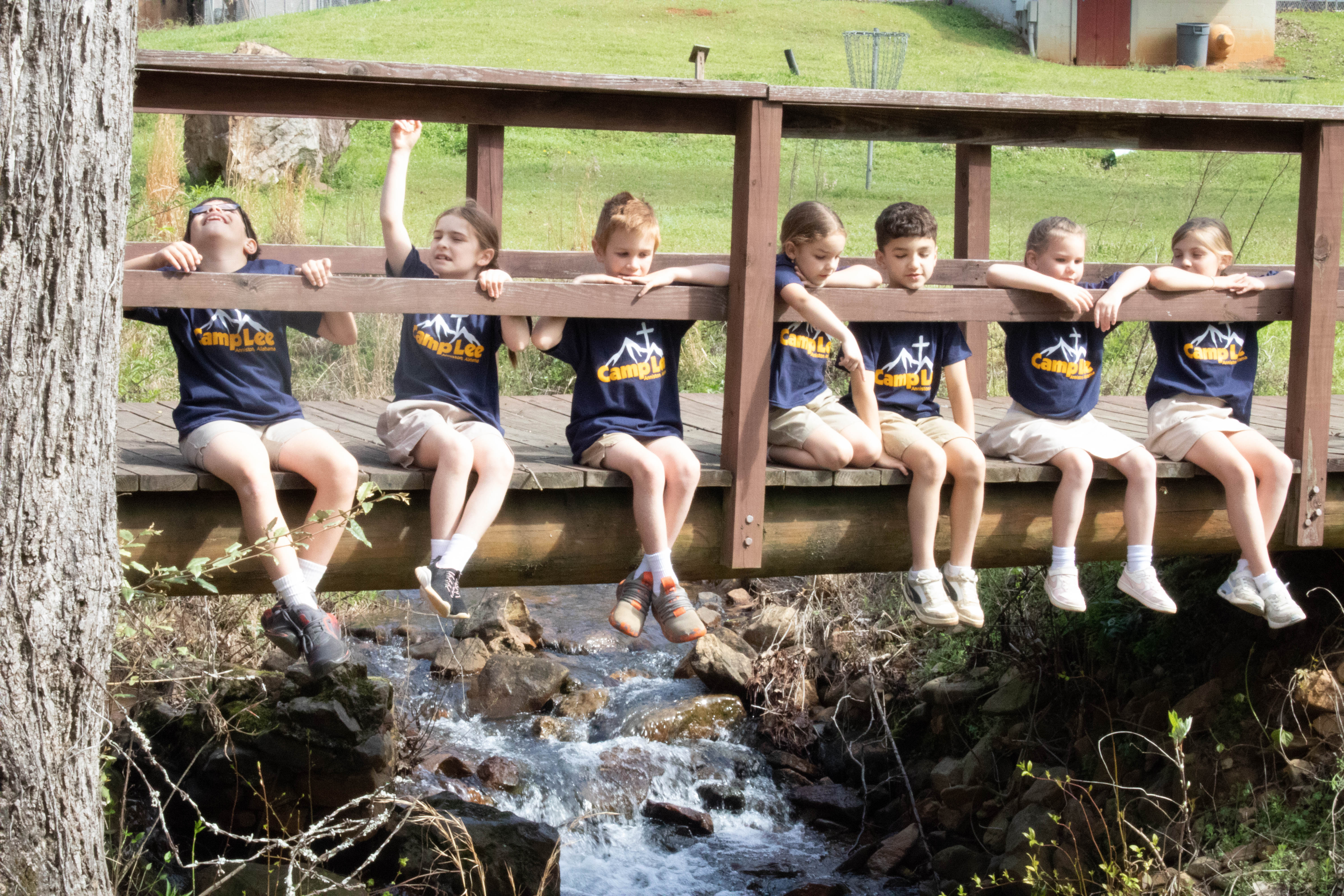 Campers sitting in a row on a wooden bridge over the creek